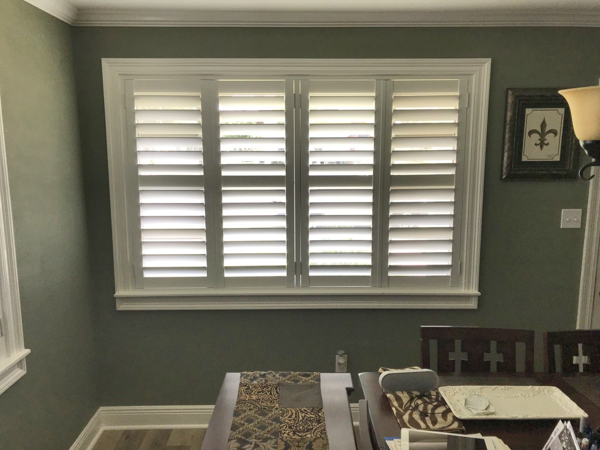 A dining room with a table and chairs and a window with white shutters