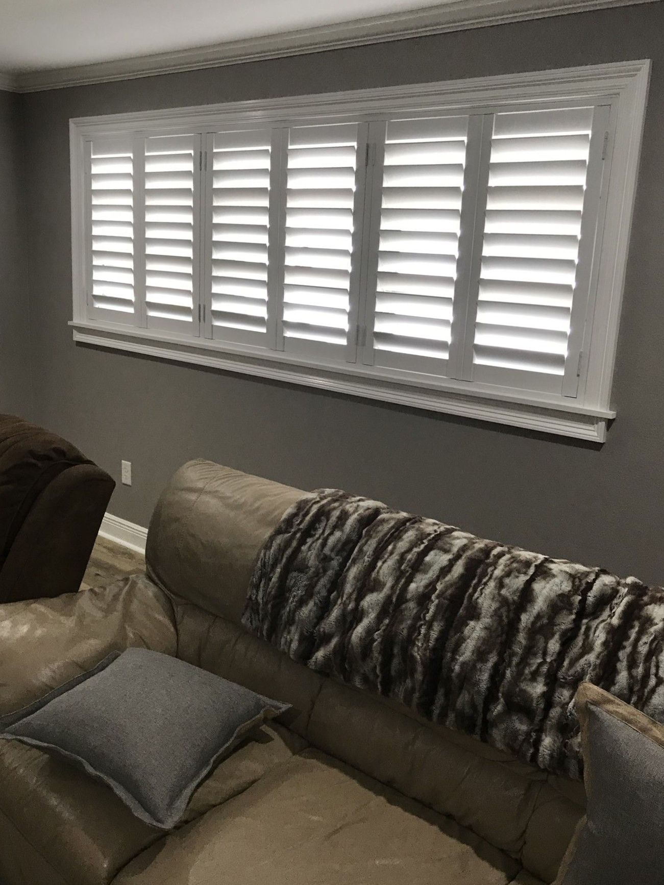 A living room with a couch and a window with shutters on it.