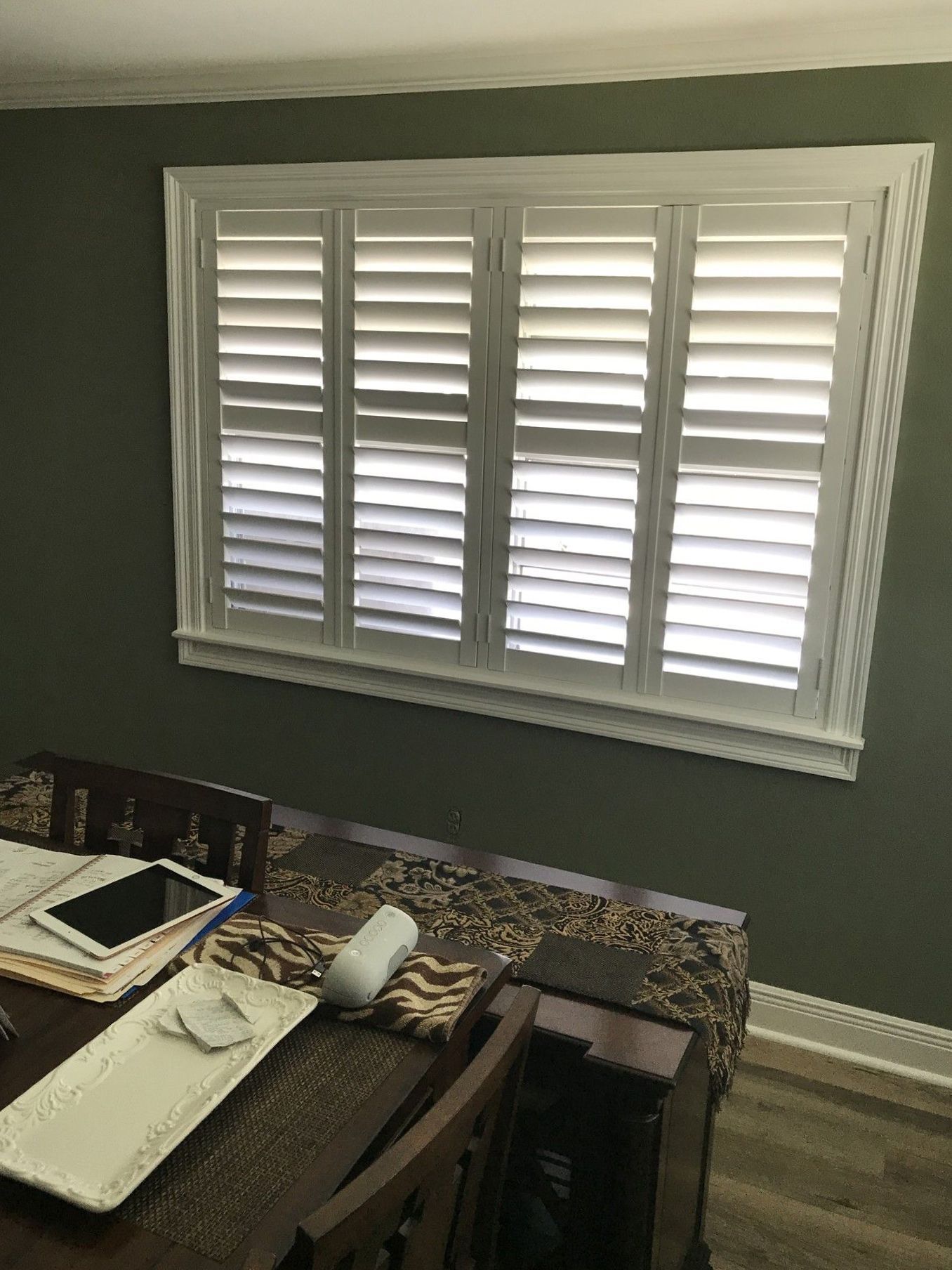 A dining room with a table and chairs and a large window with shutters.