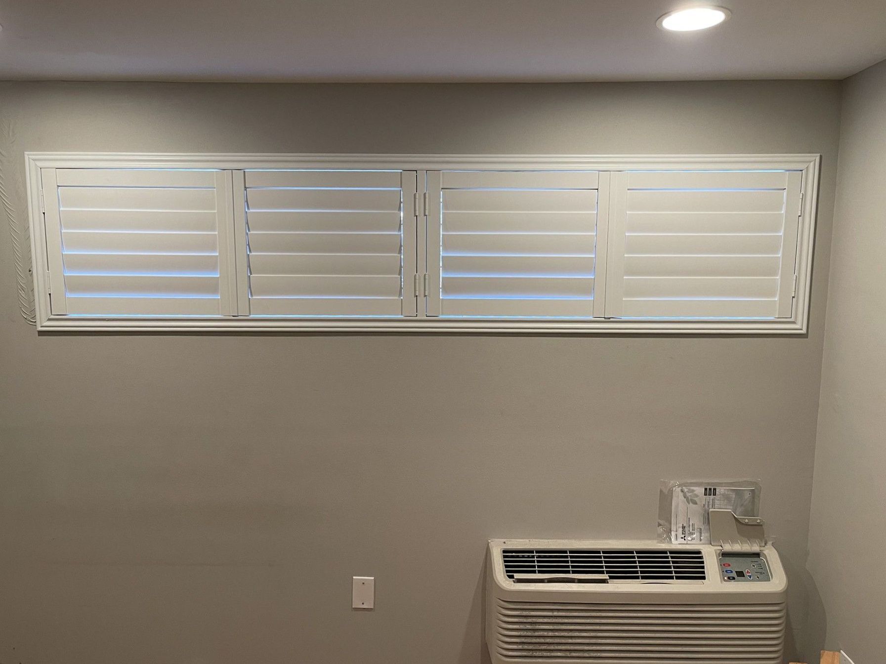 A room with a window with shutters and an air conditioner.