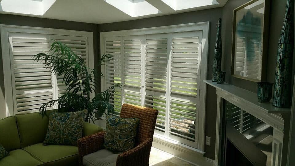A living room with a couch , chair , fireplace and shutters on the windows.