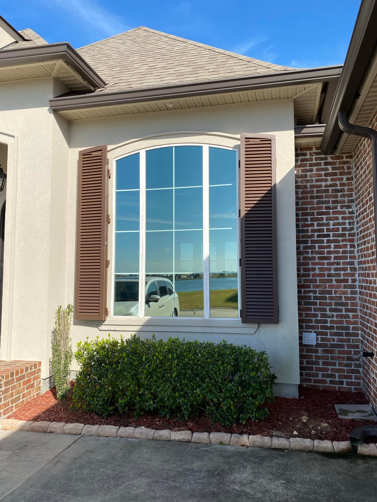 A white house with brown shutters and a large window.