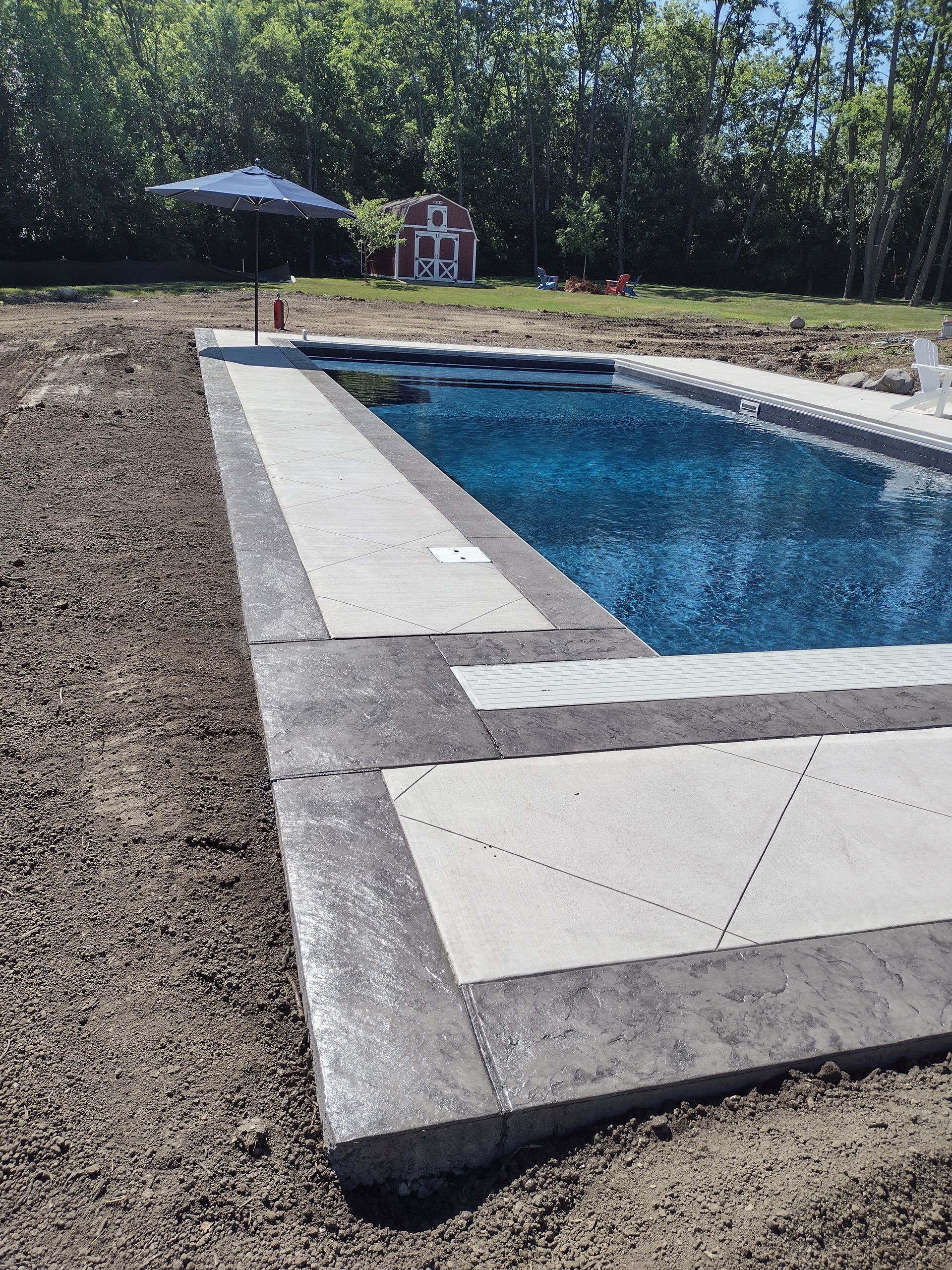 A large swimming pool is surrounded by dirt and trees