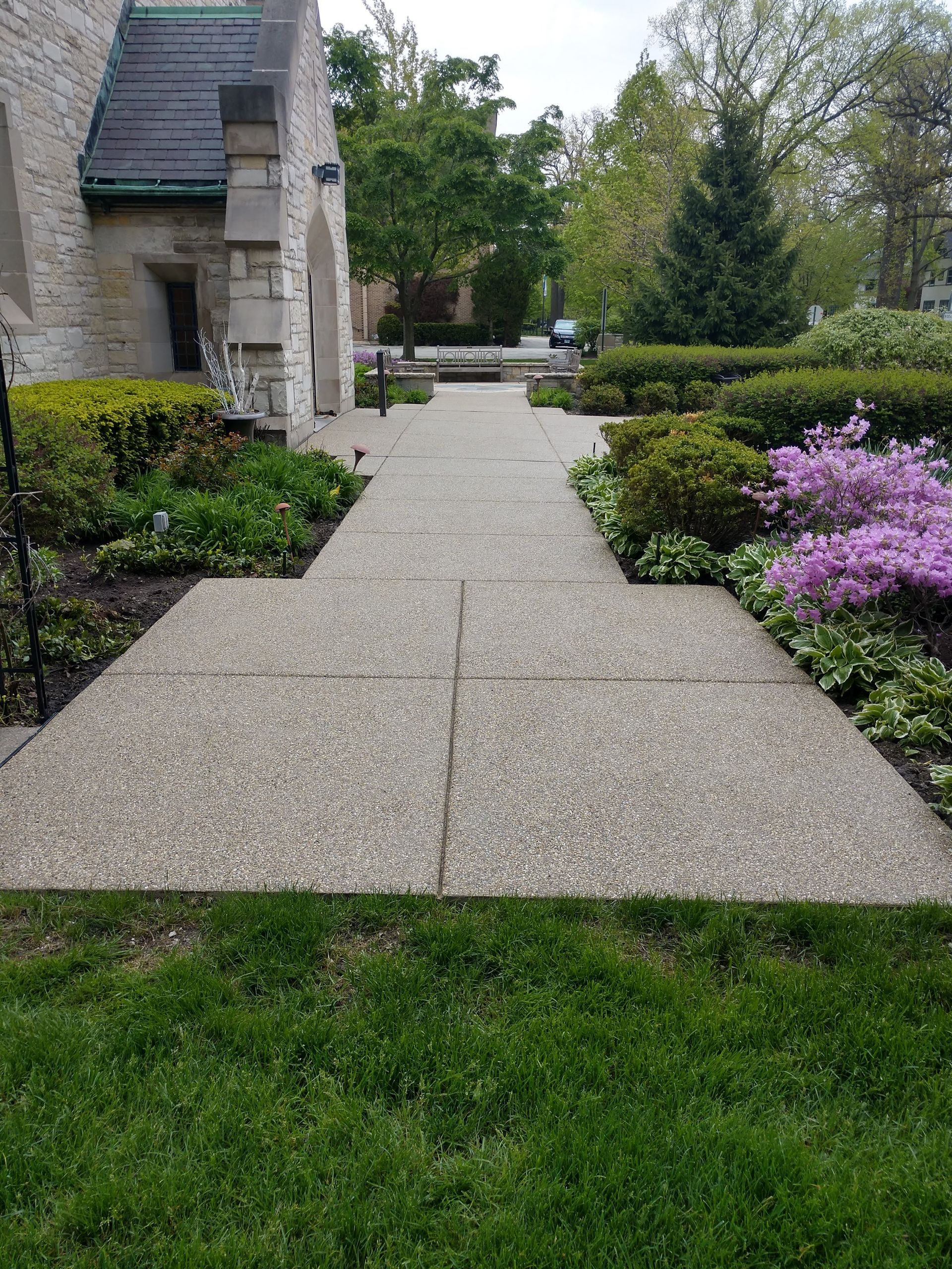 A concrete walkway leading to a building surrounded by grass and flowers.