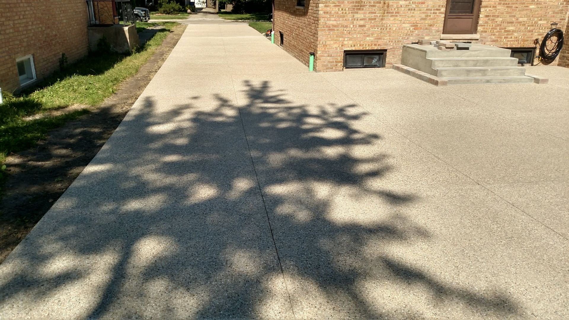 A shadow of a tree is cast on a concrete driveway in front of a brick house.