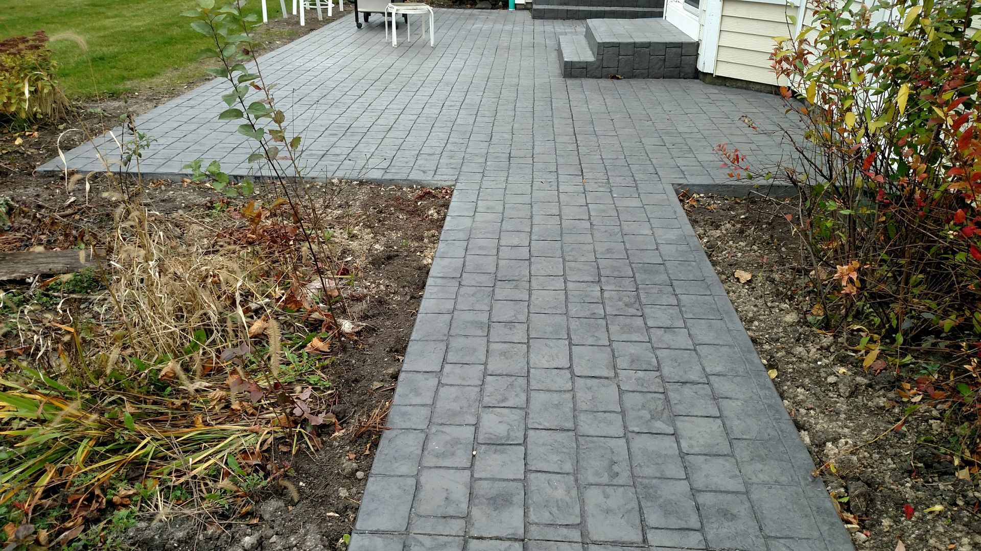 A brick walkway leading to a patio next to a house.