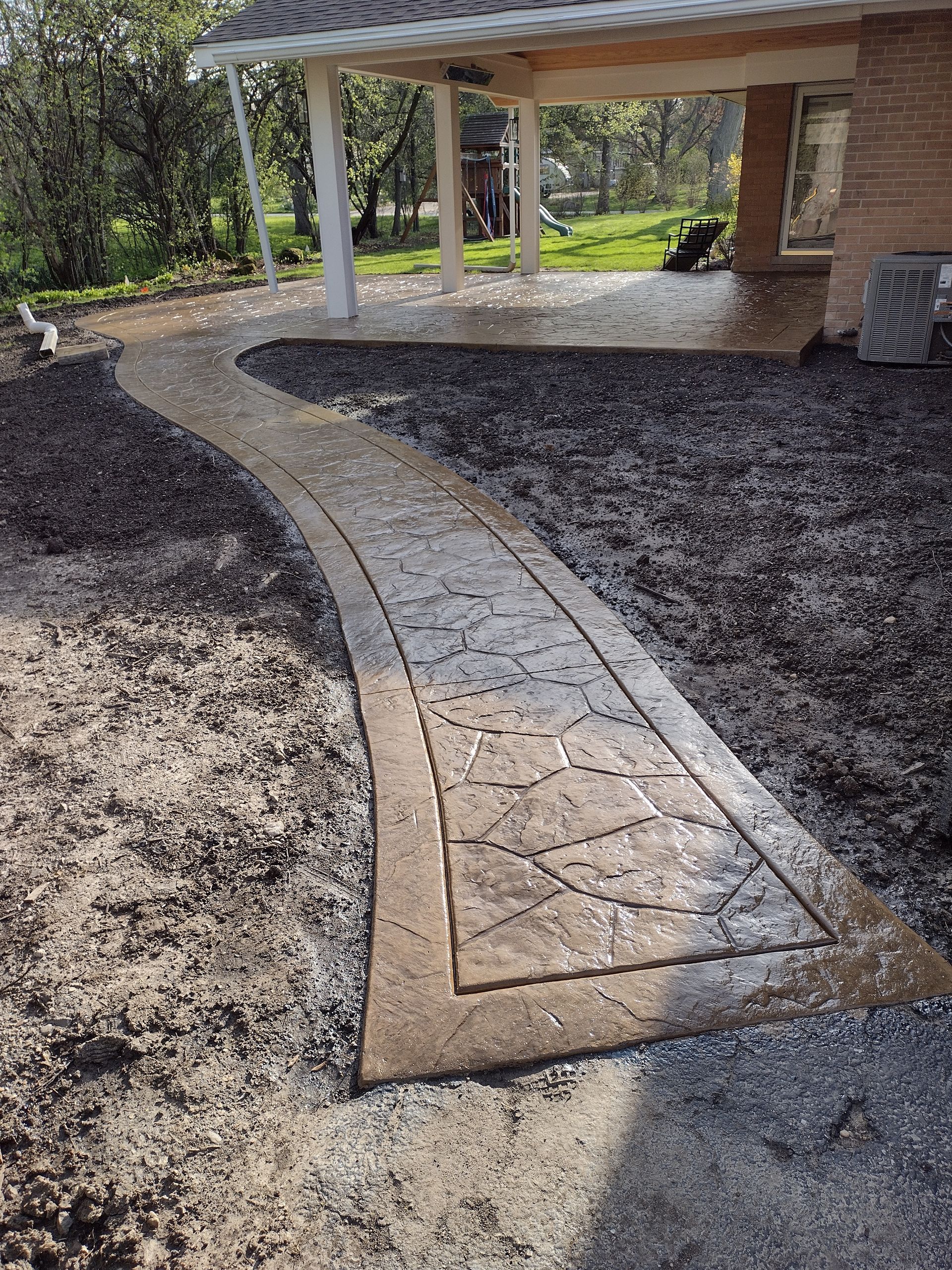 A concrete walkway leading to a house with a porch.