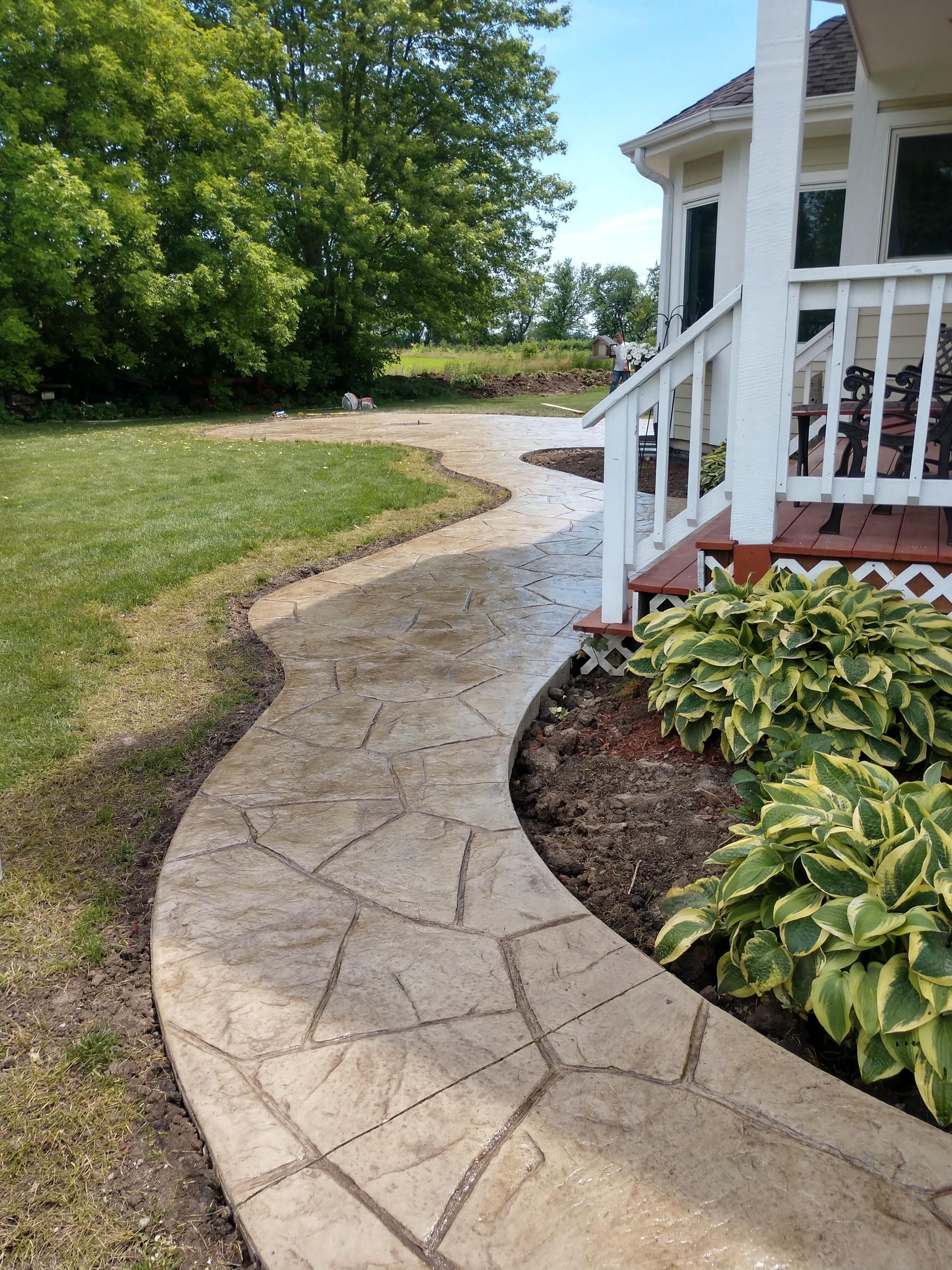 A concrete walkway leading to a house with a porch and stairs.