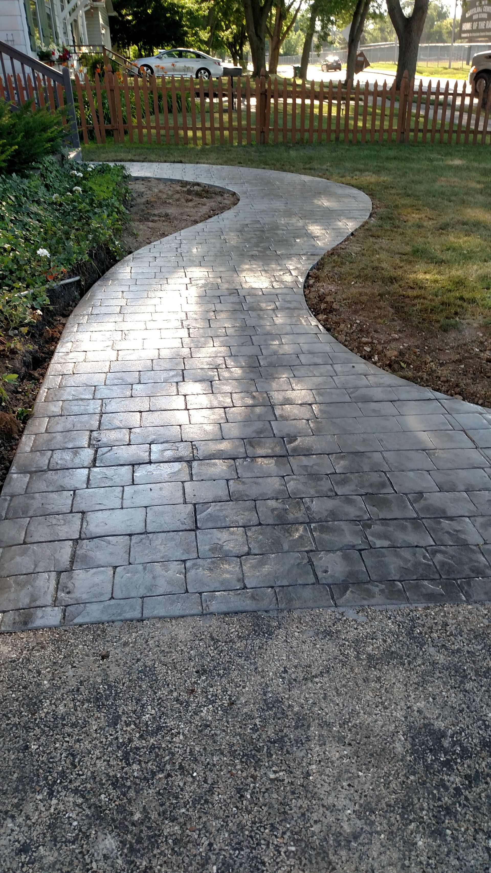 A brick walkway leading to a fence in a yard.