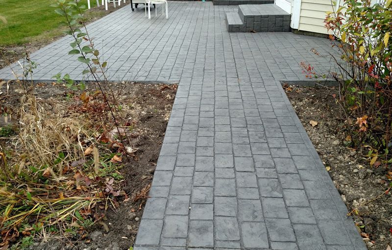 A brick walkway leading to a patio next to a house.