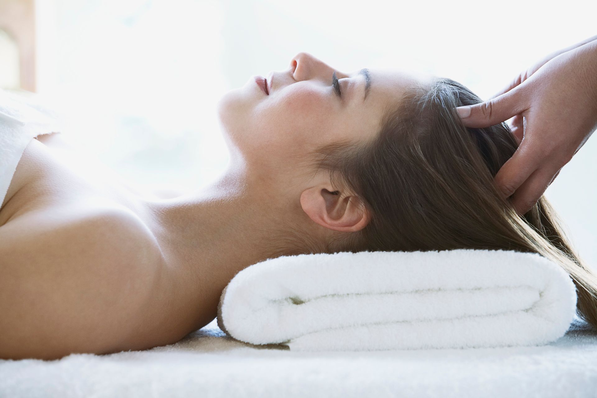 Person receiving a head massage while lying on a white towel in a spa setting