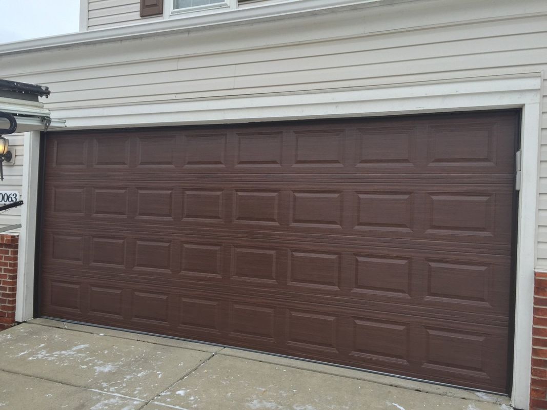 A brown garage door is sitting on the side of a house.