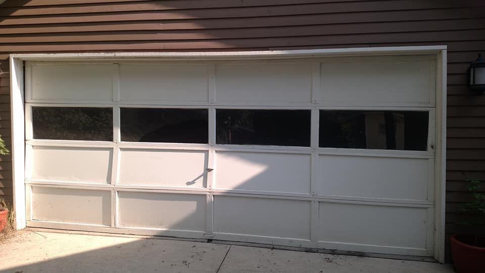 A white garage door is sitting in front of a brown house.