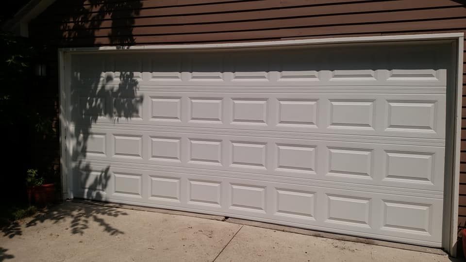 A white garage door is sitting in front of a brown house.
