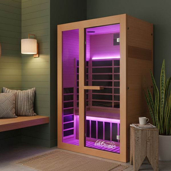 A modern wooden sauna with purple interior LED lighting, placed in a room with a bench, wall light, and a potted plant.