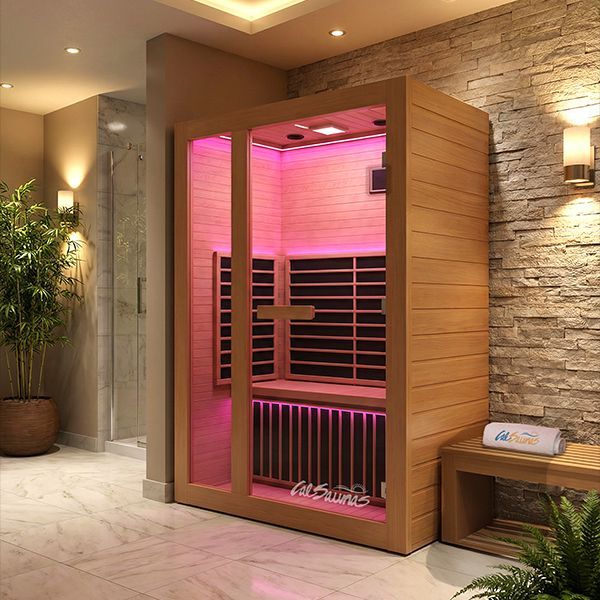 A wooden infrared sauna with pink interior lighting, positioned in a modern room with stone walls and marble tile floors.