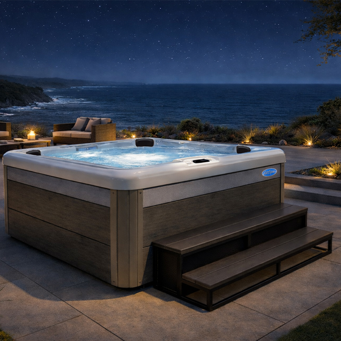 Lit hot tub on a patio at night, overlooking the ocean with a sofa in the background