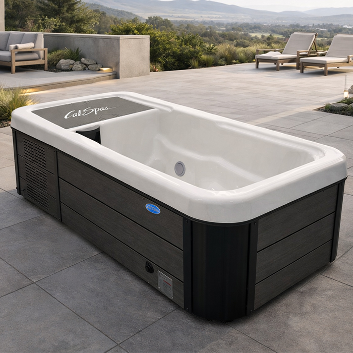 Modern outdoor hot tub with white interior and dark wood paneling on a patio with lounge chairs