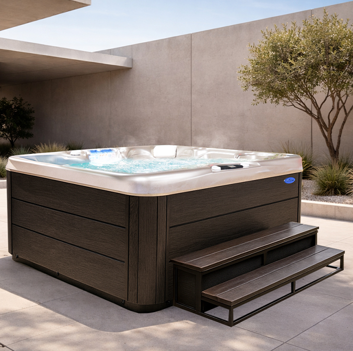 Outdoor hot tub with built-in steps on a patio beside a stucco wall and tree