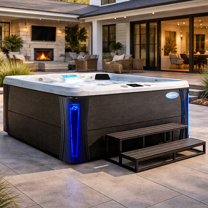 Large lit hot tub with steps on a modern patio at dusk, outside a house with a fireplace