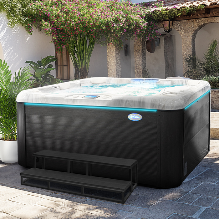 Black outdoor hot tub with cover on a stone patio beside a house and vines