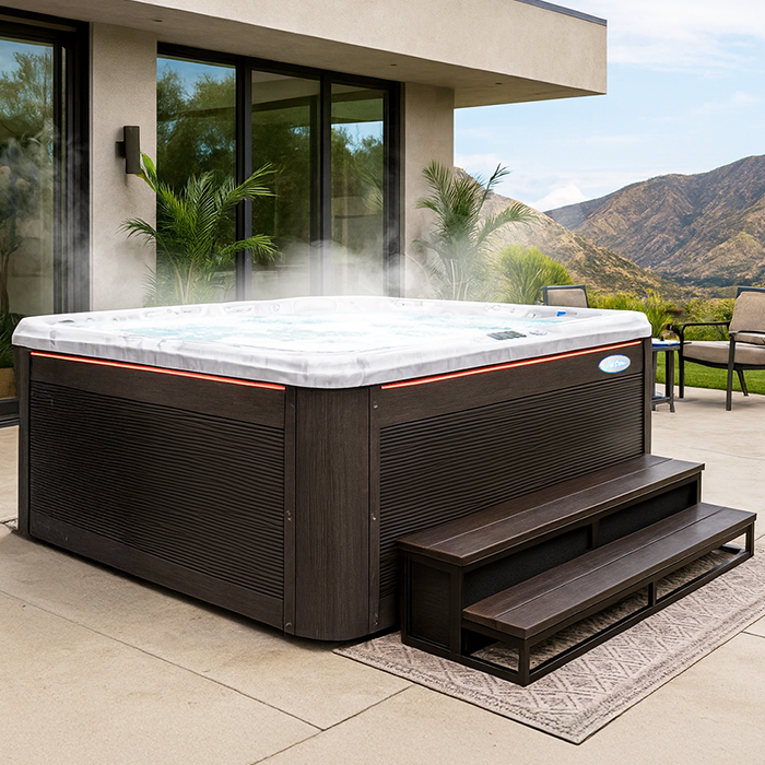 Large brown hot tub with steps on a patio beside a modern house, with mountains in the background