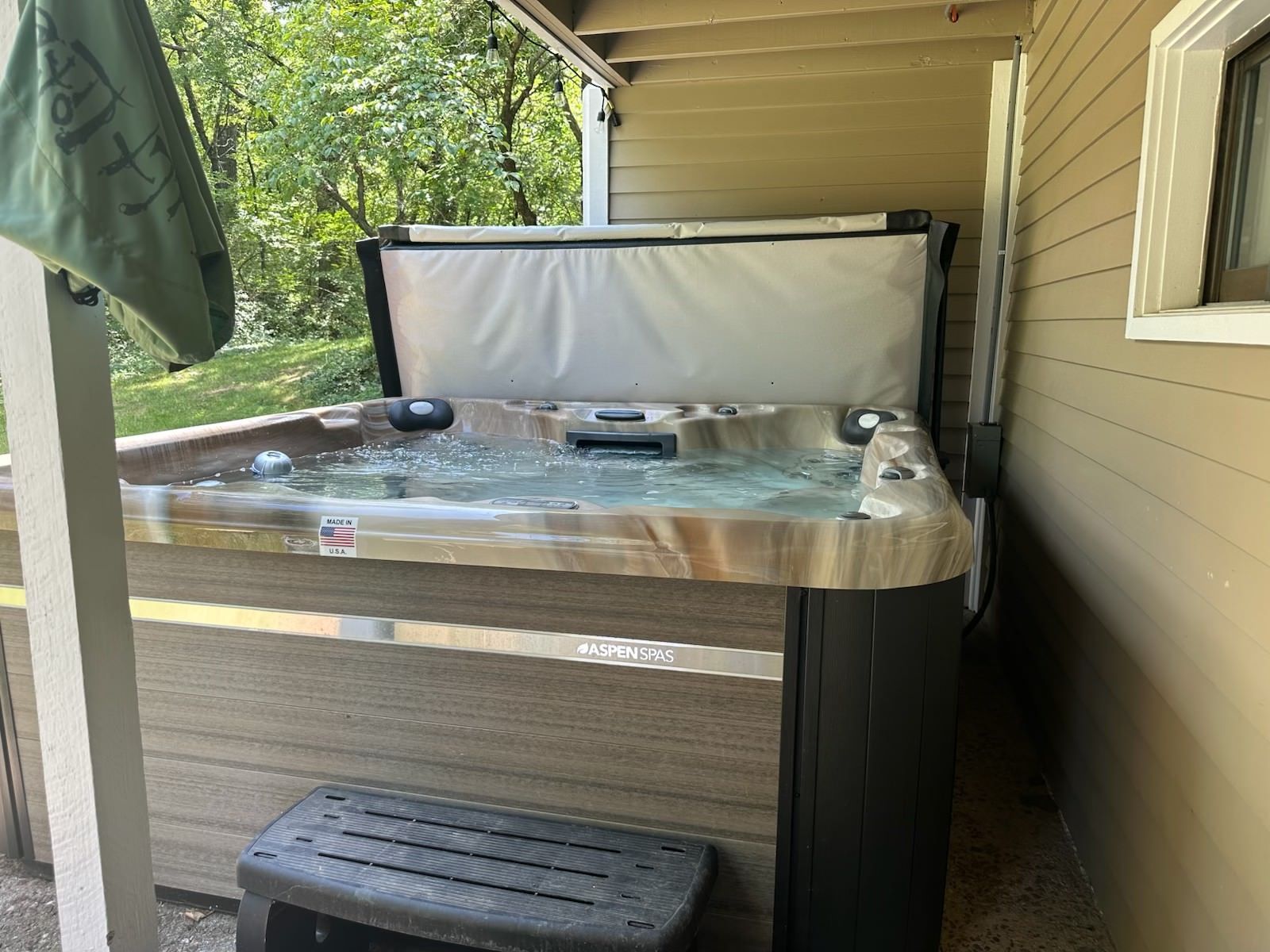 A hot tub with cover open, next to a building on a deck.  Bubbles are visible in the water.