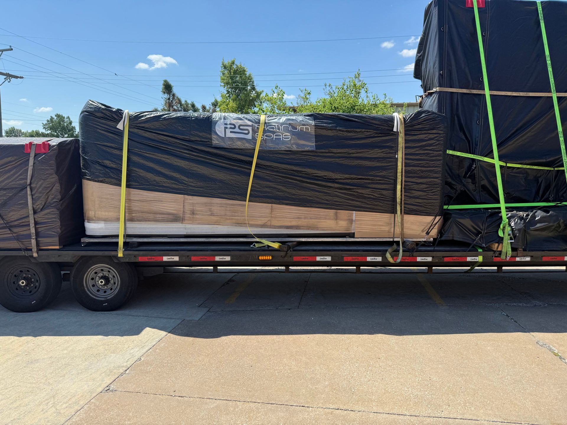 Flatbed trailer loaded with lumber wrapped in black tarp, secured with straps.
