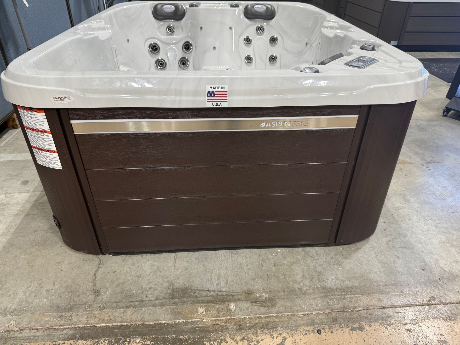 Brown and gray hot tub, with jets, on a concrete floor.