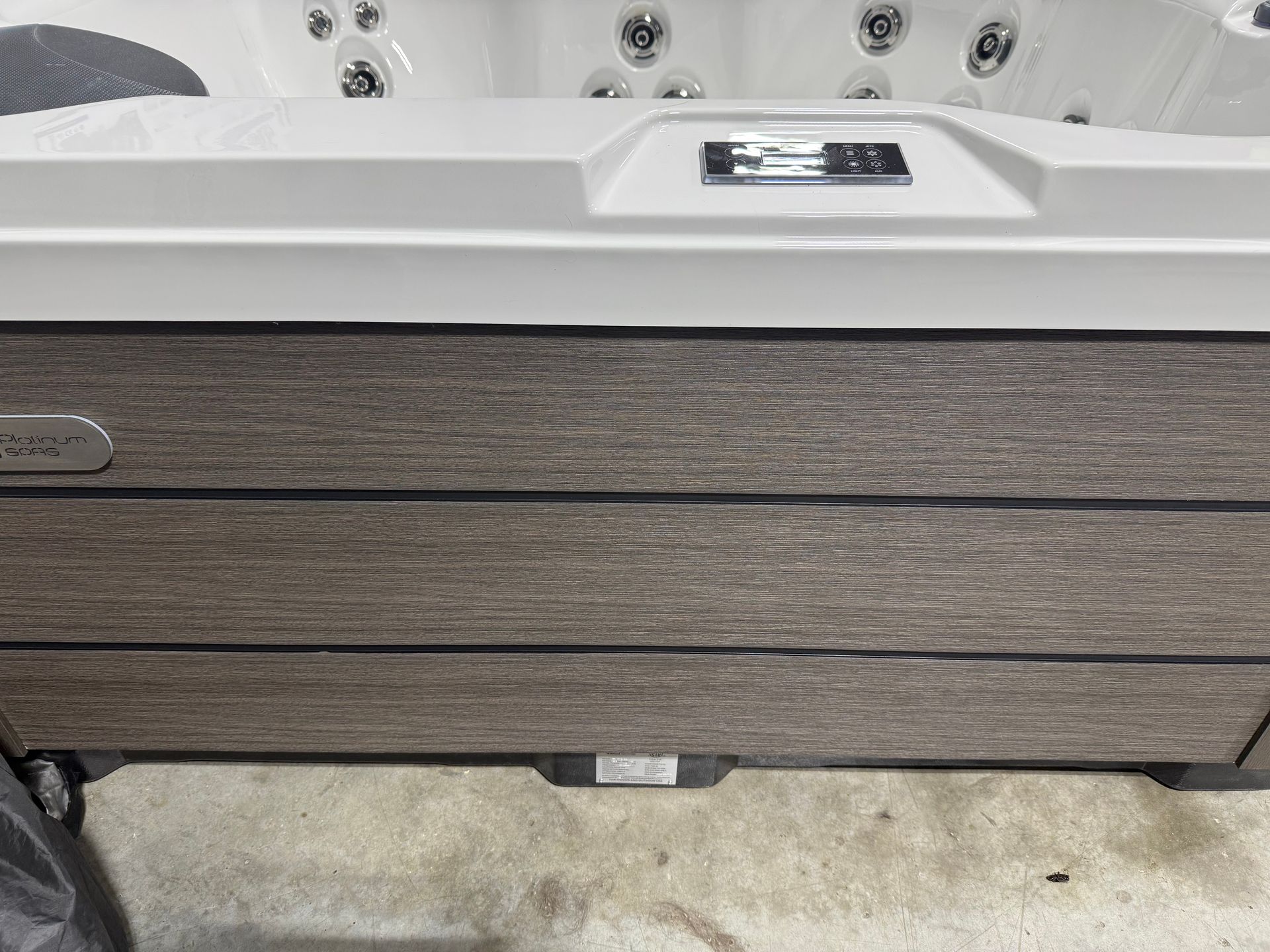 Hot tub with gray and brown paneling. Top features control panel and jets.