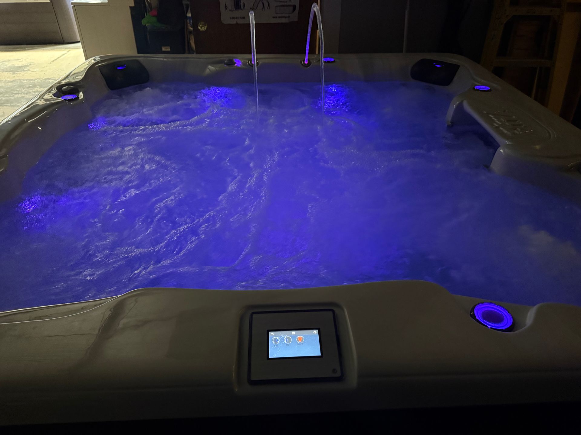 A lit-up hot tub with blue water. Control panel in front, jets creating bubbles.
