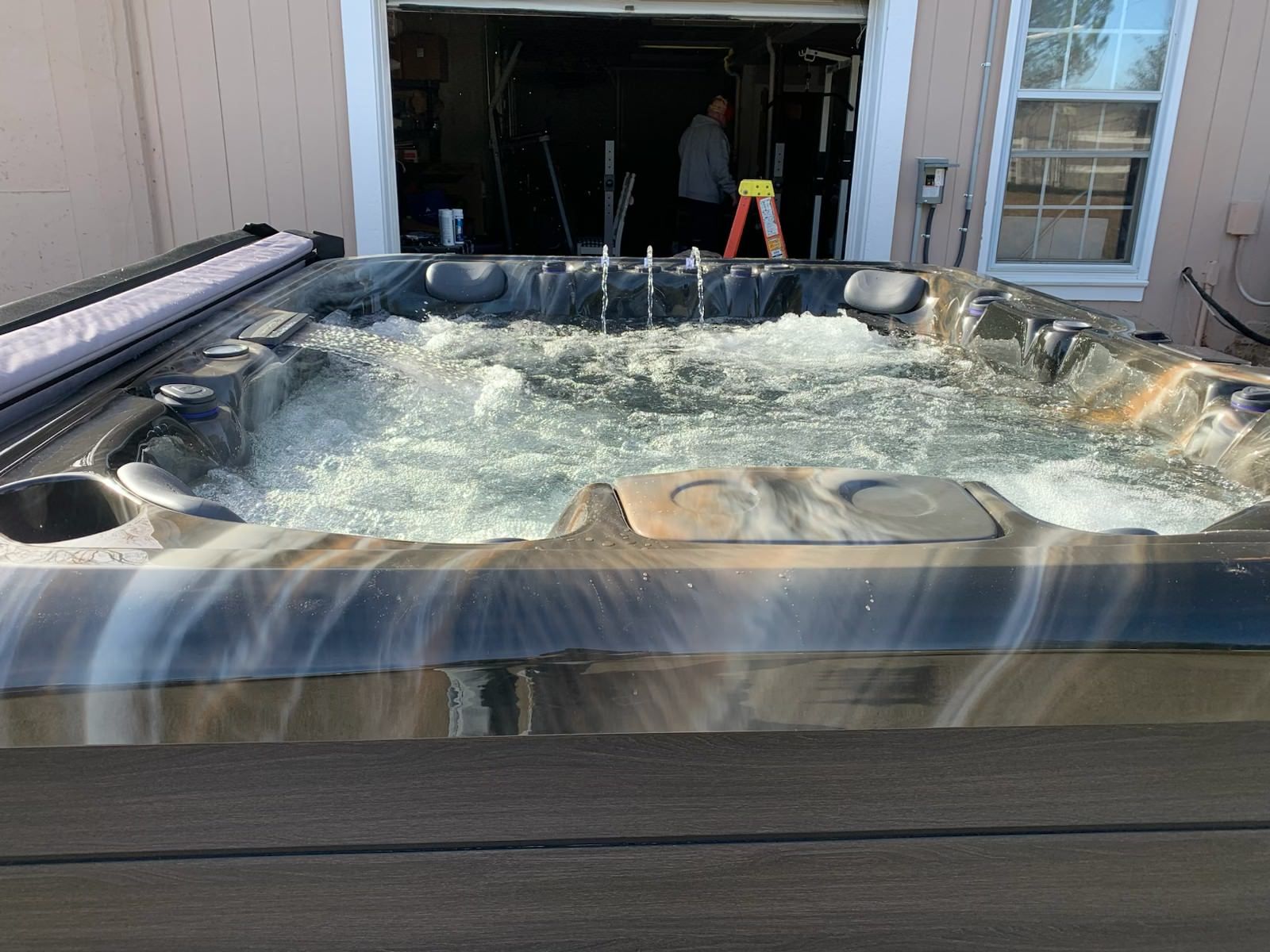 Hot tub with bubbling water outdoors; garage and person in background.