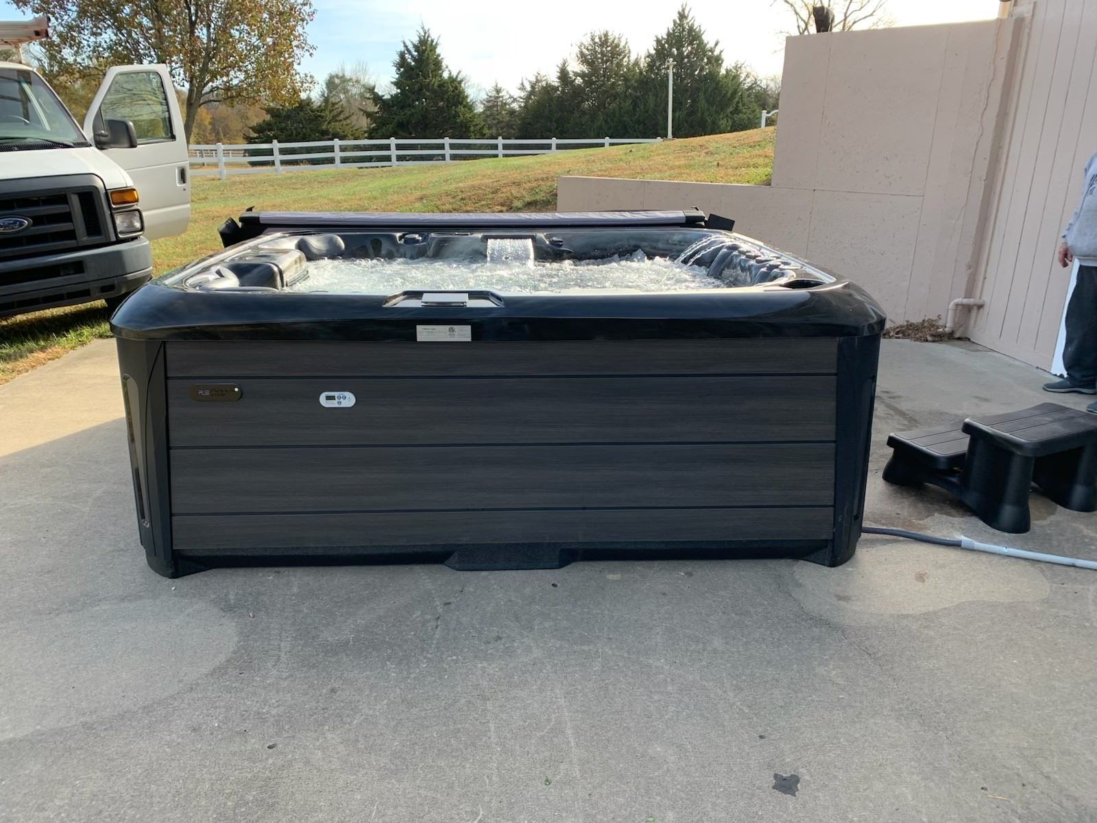 Black hot tub on concrete patio with bubbles, near a van and building.