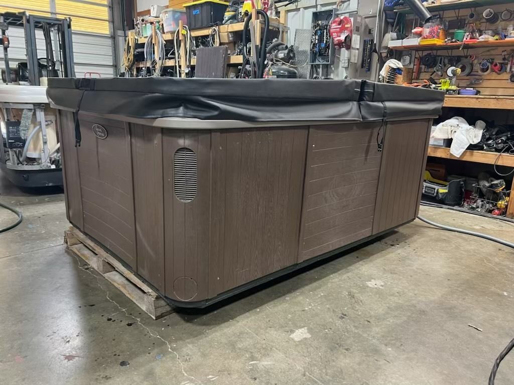 A brown hot tub with a black cover, on a pallet, inside a cluttered workshop.
