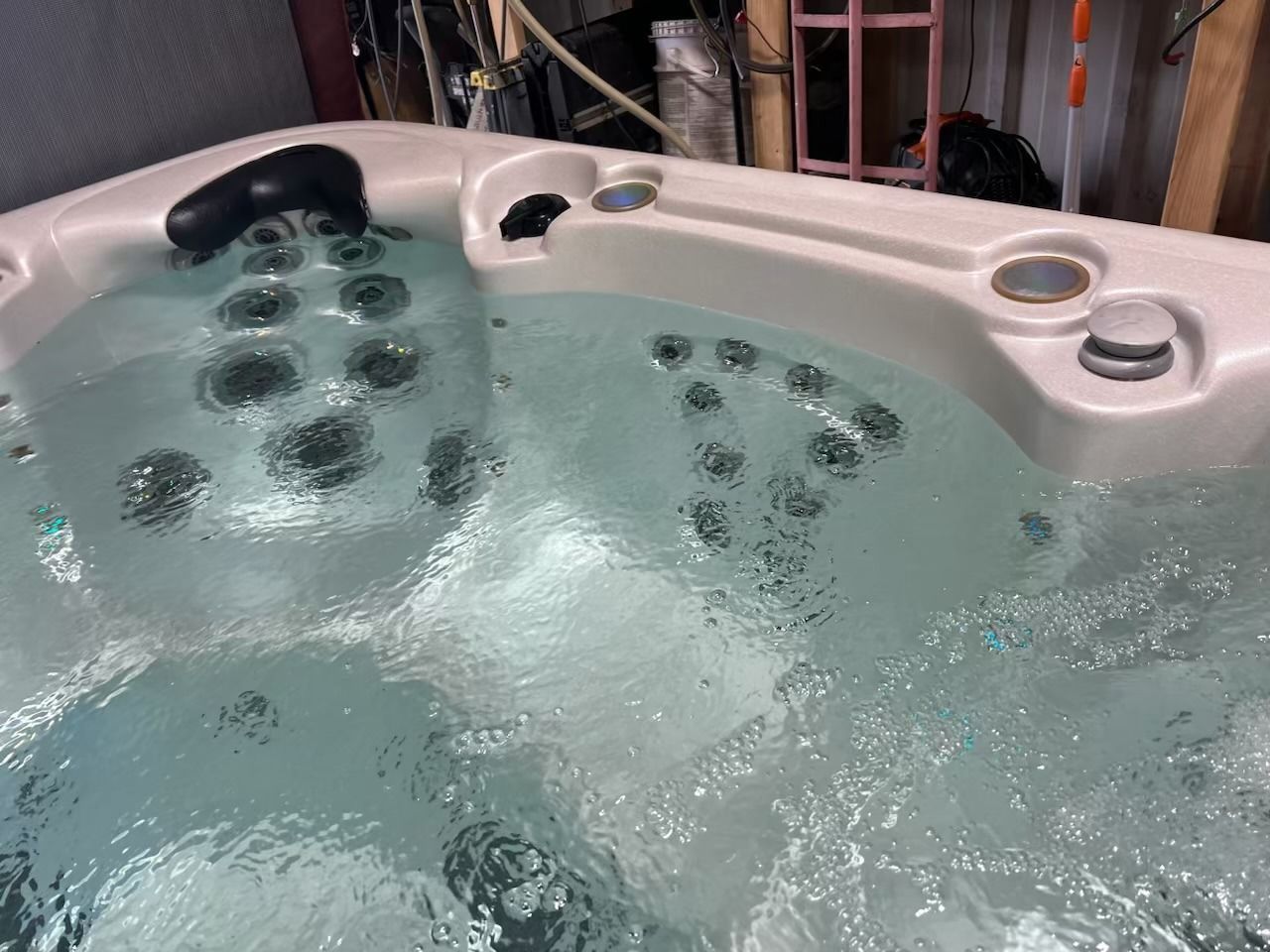 Hot tub filled with bubbly water, jets visible. White surround, black headrest.