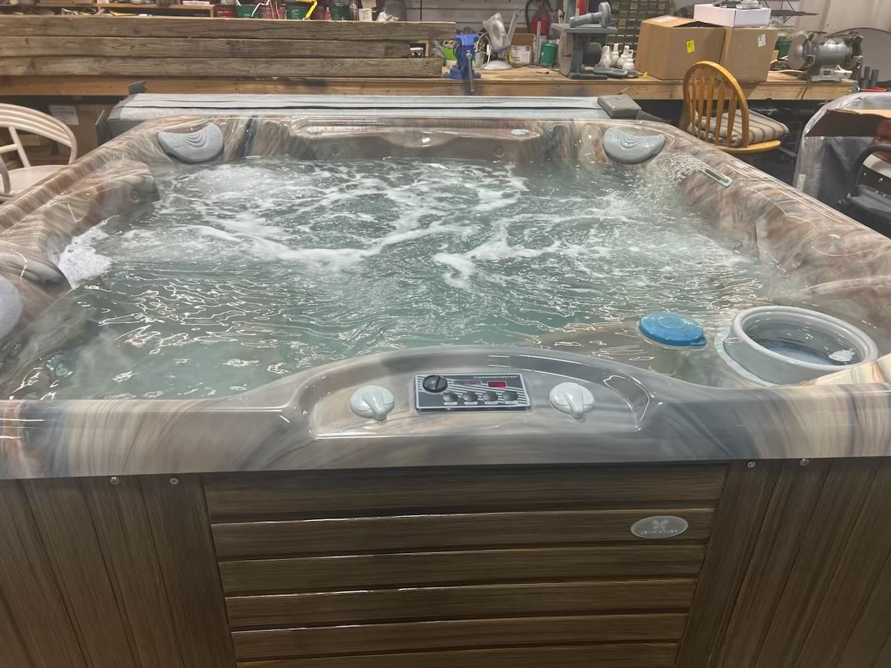 A bubbling hot tub with a control panel is indoors, lit by overhead lighting.