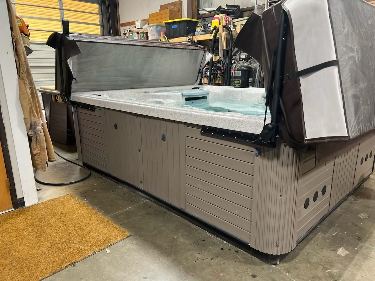 A large, open hot tub with partially-opened cover inside a garage. The tub is brown with gray trim.