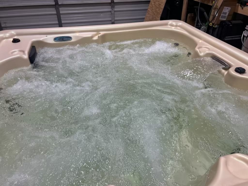 Bubbling hot tub with tan interior and jets, water is foamy, in a garage.
