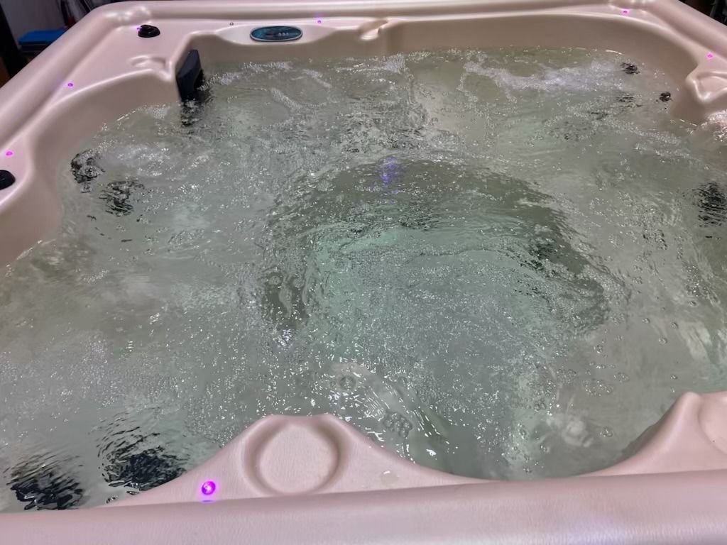 A hot tub filled with bubbling water, beige interior, some lights visible.