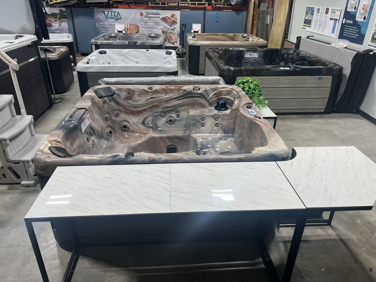 Hot tubs displayed in a showroom. A brown, marble-like tub has a tile tabletop attached. Other tubs are in the background.