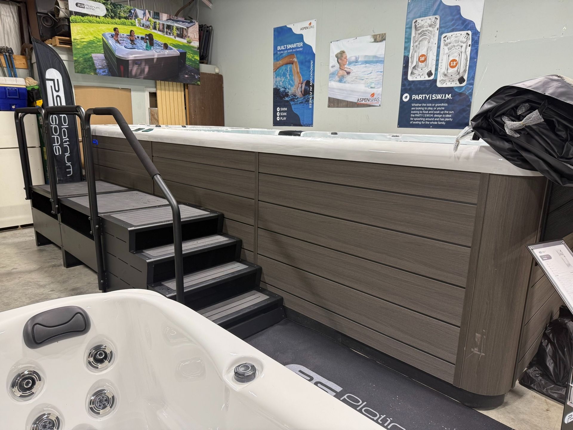 A swim spa with gray steps and handrails. Another white spa is in the foreground.