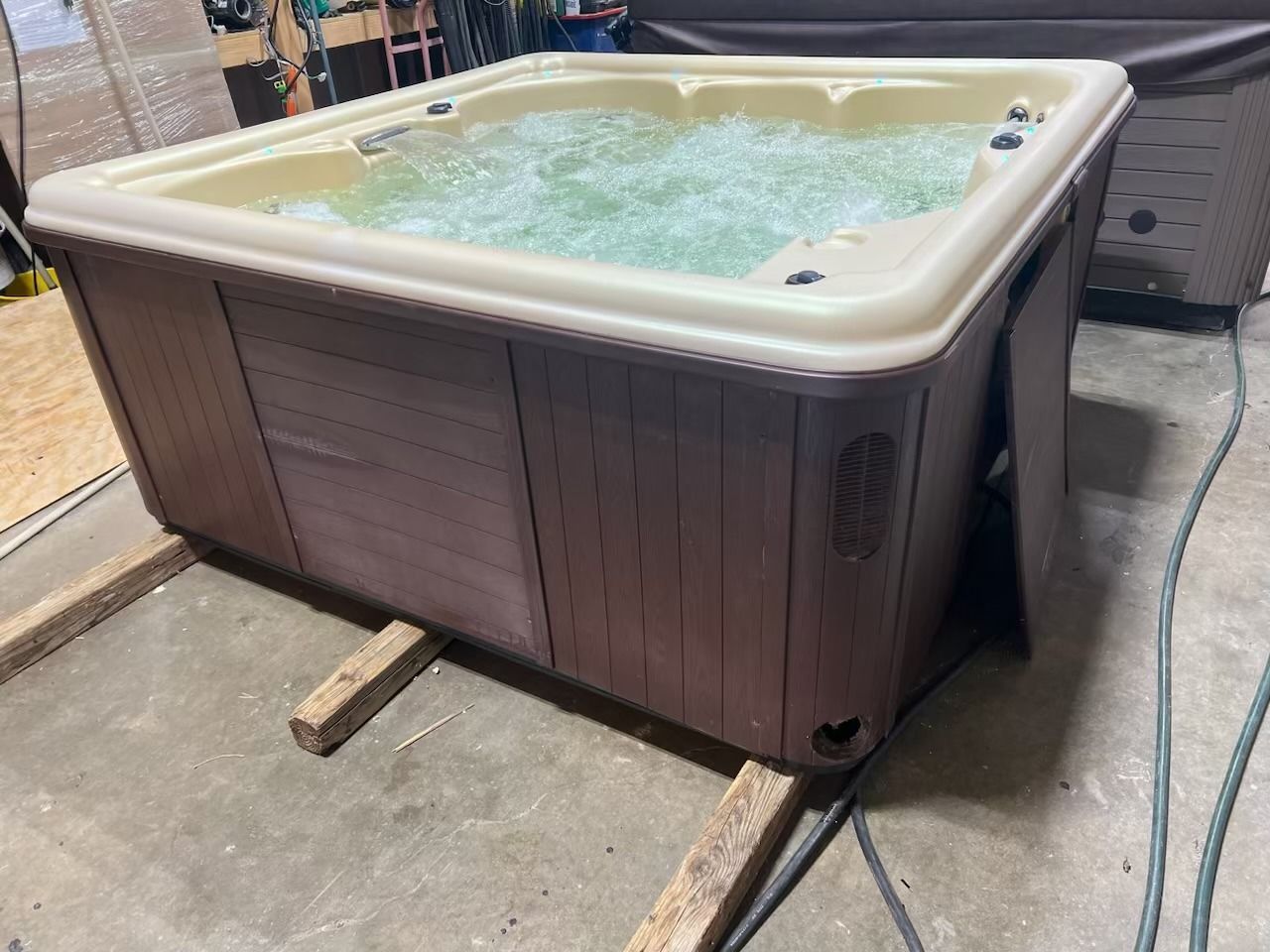 A brown and tan hot tub with bubbling water, resting on wooden supports in a garage.