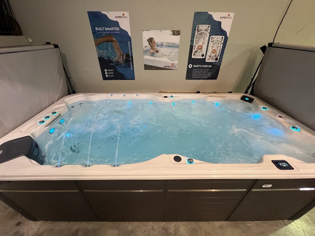 Hot tub filled with blue water, surrounded by gray panels and posters on a wall.