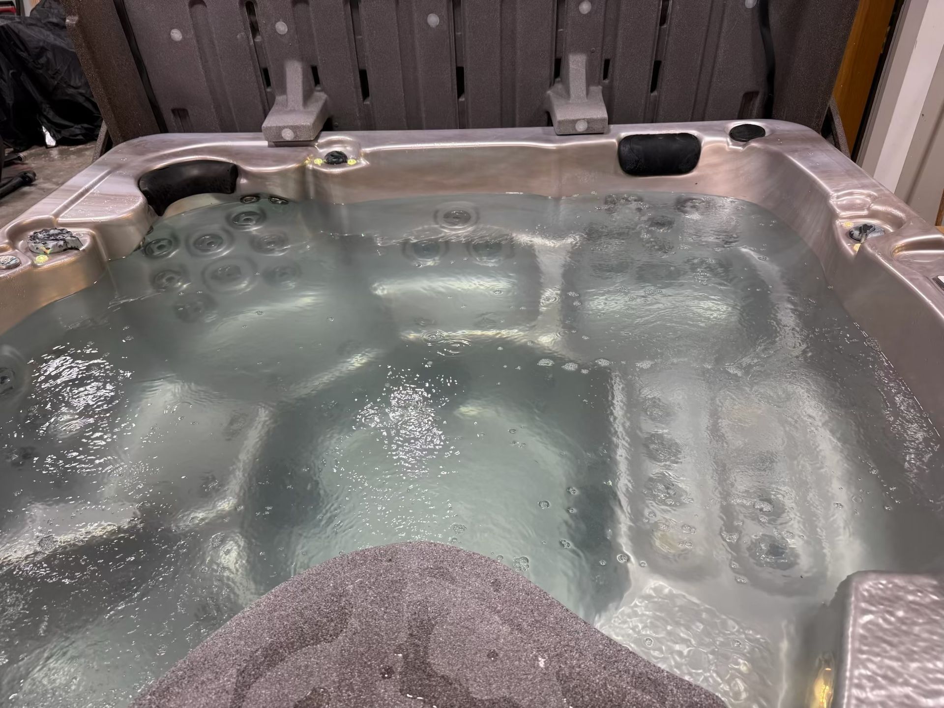 Hot tub filled with water, jets on. Gray exterior, gray stone in foreground.