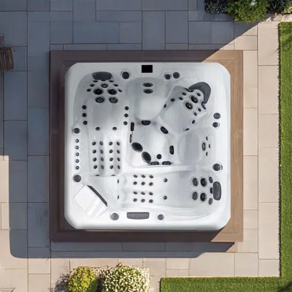Top-down view of a white, multi-seat hot tub with numerous jets, installed on a patio beside a grassy lawn.