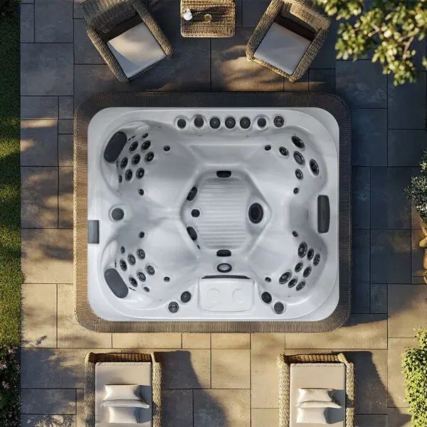 Overhead view of a square, white hot tub on a stone patio, surrounded by four wicker chairs and a small table.