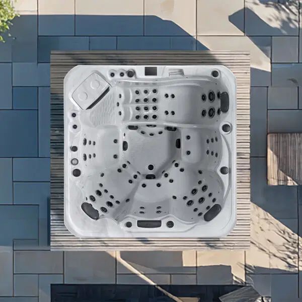 Top-down view of a white, multi-seat hot tub with built-in jets, installed on a wooden deck surrounded by stone pavers.