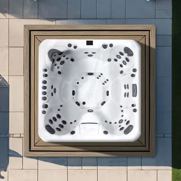 An overhead view of a square white hot tub with multiple jets, set into a wooden deck on a stone patio.