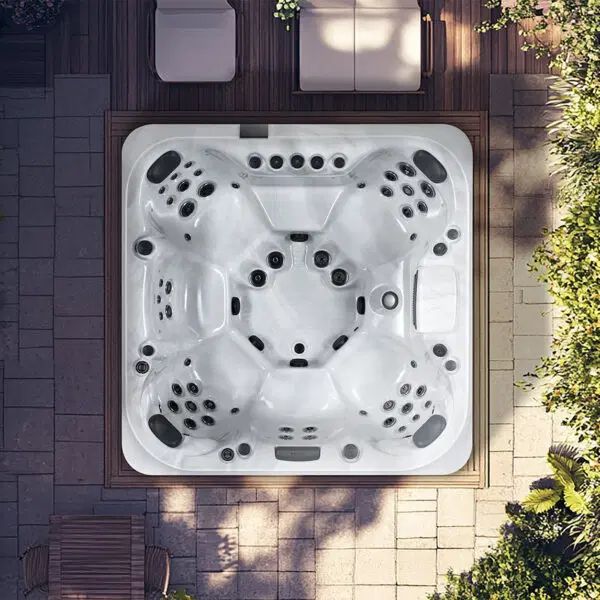 Top-down view of a white, multi-seat hot tub installed in a stone patio area near plants and patio furniture.