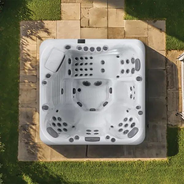 A white square hot tub with multiple jets and seating, situated on a stone patio surrounded by grass from a top-down view.